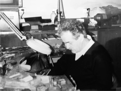 An archival portrait of a jeweller working at his bench beneath a workshop lamp